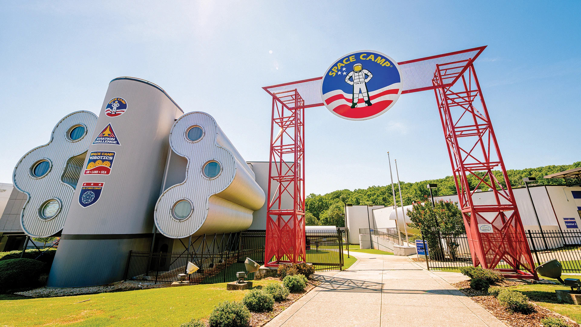 Red gates with Space Camp logo at top. The entrance is next to the habitat student dorms.
